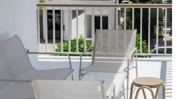 A balcony with a white metal chair, a wooden stool, and a white metal table.