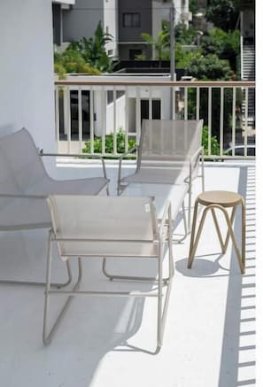 Ein Balkon mit einem weißen Metallstuhl, einem hölzernen Hocker und einem weißen Metalltisch.