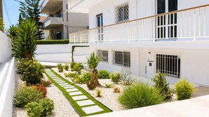 Un edificio de varios pisos con balcones, un sendero pavimentado y diversas plantas.