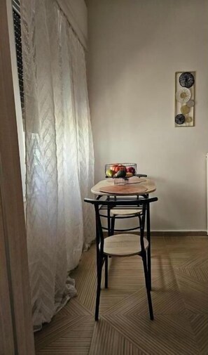 Ein Zimmer mit Esstisch und Stühlen, einem Fenster mit Vorhängen sowie einer Wanddekoration.