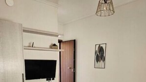 Un dormitorio con una cama, un televisor montado en la pared, una puerta y una lámpara colgante.