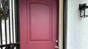 Una puerta roja con una reja de metal y un muro de ladrillo blanco.