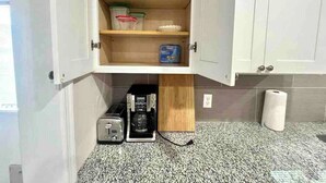 Una cocina con cafetera integrada, tostadora y estante con recipientes.