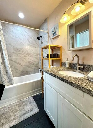 A bathroom with a bathtub, a sink with a granite countertop, and a showerhead. - Restful Retreat w/Smart TV & Free Parking near NRG (Houston)