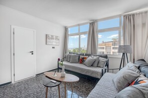Ein stilvolles Wohnzimmer mit einer Couch, einem kleinen Tisch und einem Fenster mit Vorhängen.