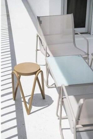 Ein Balkon mit einem weißen Metallstuhl und einem kleinen, runden Hocker.