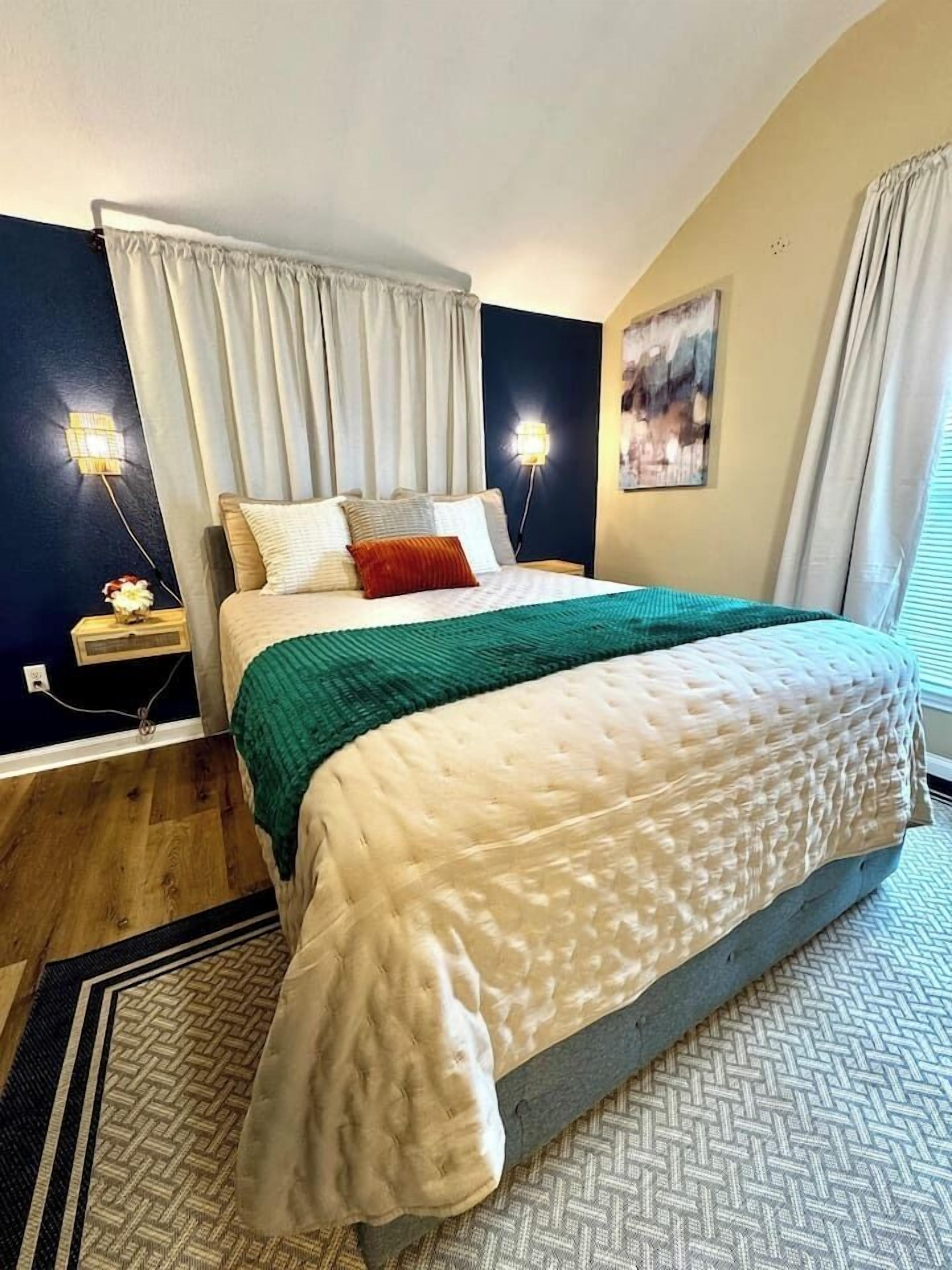 Ein Schlafzimmer mit einem Bett, Vorhängen, einer Wandleuchte und einem Bild.