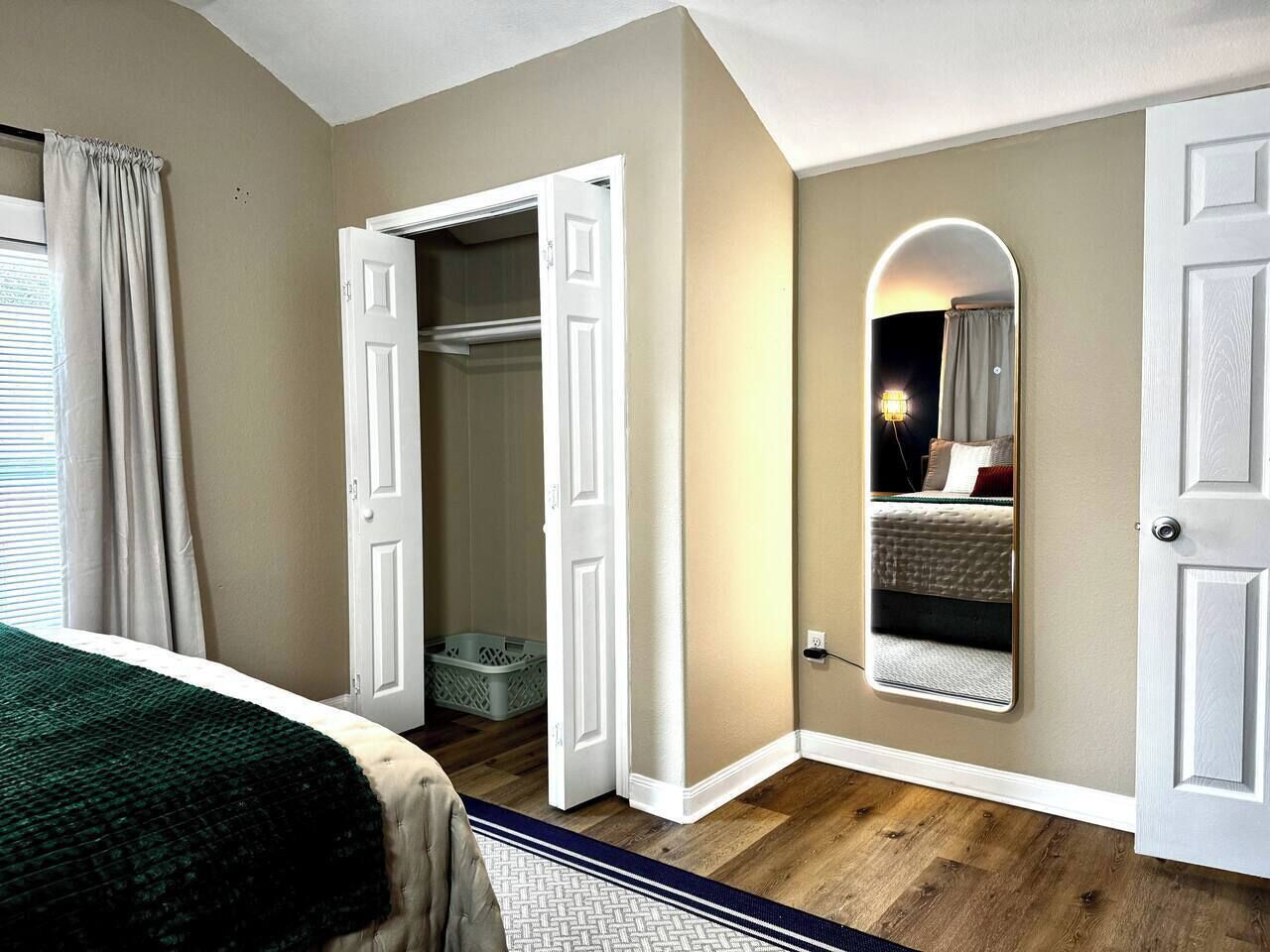 A bedroom with a bed, a closet, a mirror, and a door leading to another room.