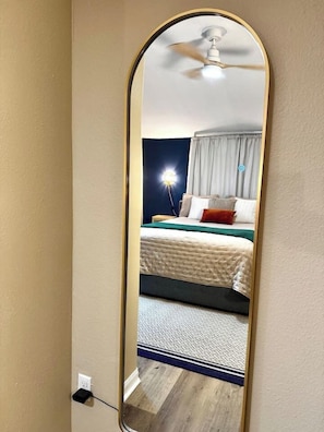 Ein Spiegelbild zeigt ein Schlafzimmer mit Bett, Vorhängen und Deckenventilator.