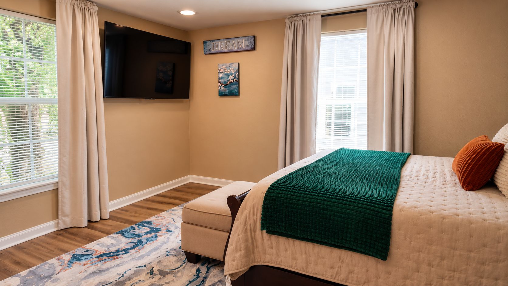 A bedroom with a bed, a television mounted on the wall, and a window with curtains.