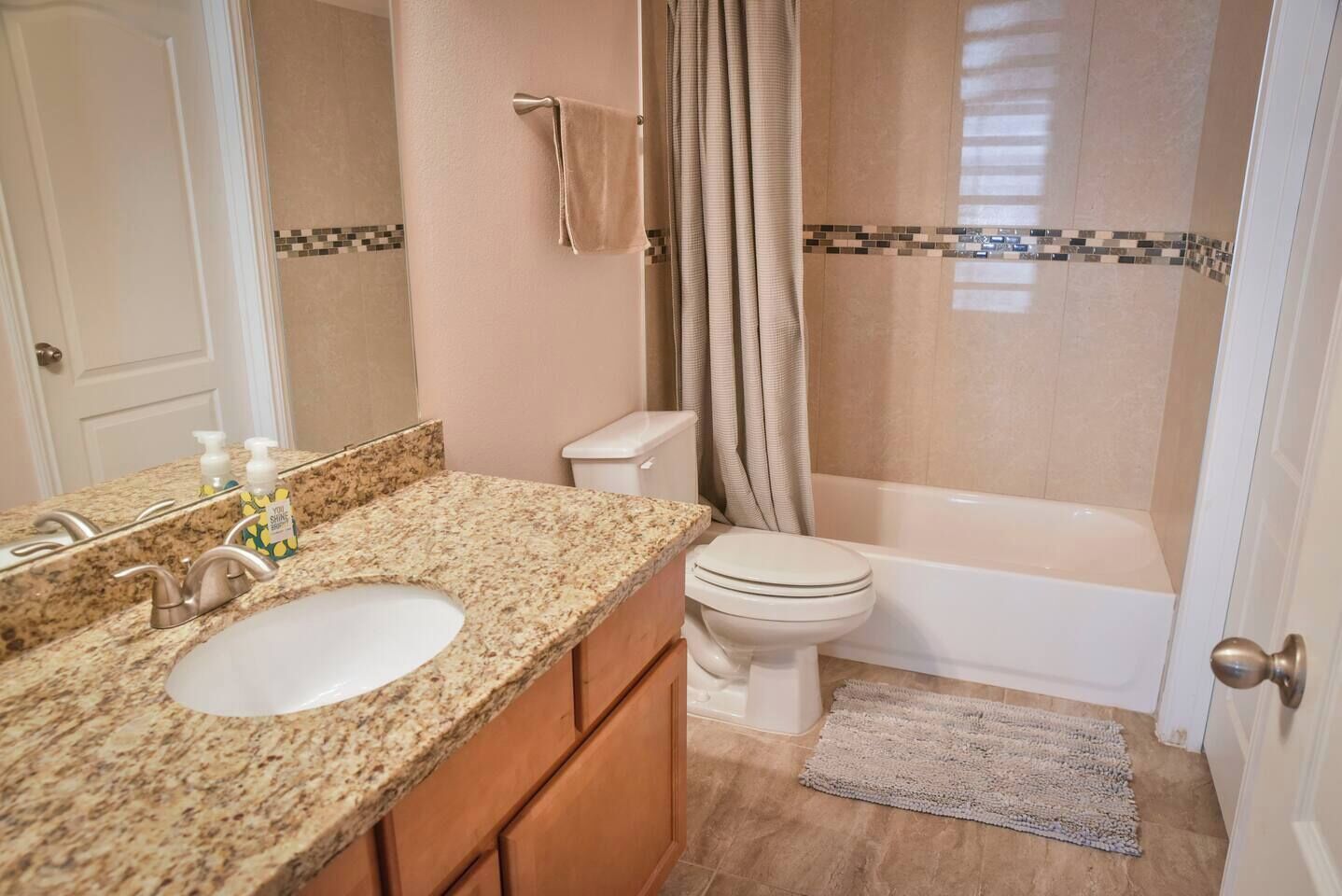 Ein Badezimmer mit Granitwaschtisch, Toilette, Badewanne und Duschvorhang.