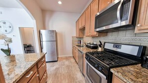 A kitchen with wooden cabinets, a stainless steel refrigerator, a microwave, a stove, and granite countertops. - Near NRG Houston Stay - Patio + Free Parking (Houston)