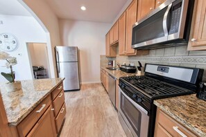 A kitchen with wooden cabinets, a stainless steel refrigerator, a microwave, a stove, and granite countertops. - Near NRG Houston Stay - Patio + Free Parking (Houston)