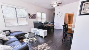 A modern living room with a sectional sofa, a glass coffee table, a white entertainment unit, and a dining area with a wooden table and chairs. - Near NRG Houston Stay - Patio + Free Parking (Houston)