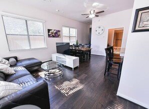 A modern living room with a sectional sofa, a glass coffee table, a white entertainment unit, and a dining area with a wooden table and chairs. - Near NRG Houston Stay - Patio + Free Parking (Houston)