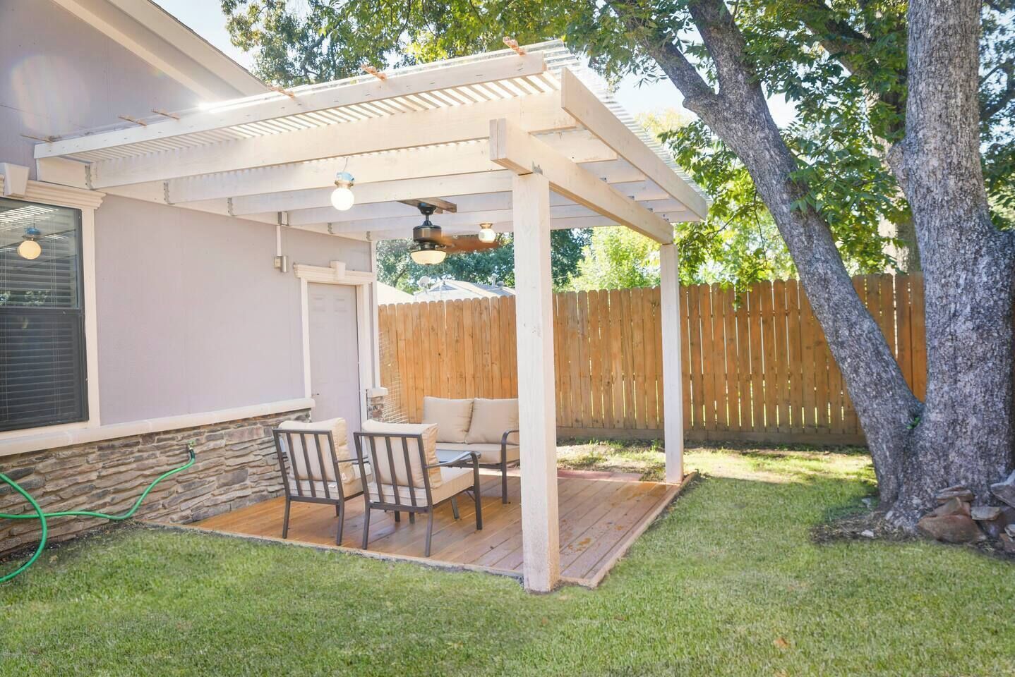 A covered patio with a table and chairs, a wooden deck, and a stone wall.