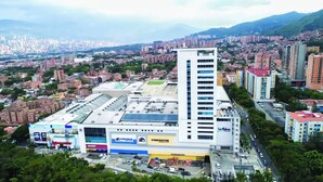 A large commercial building with multiple floors, a prominent vertical structure, and a parking lot with various vehicles. - VIP Nomad Nest in New PH With Air C, Kitchen, Steps to Metroplus (Medellín)