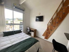 Ein Schlafzimmer mit Bett, Schreibtisch, Stuhl, Fernseher und einer Treppe.