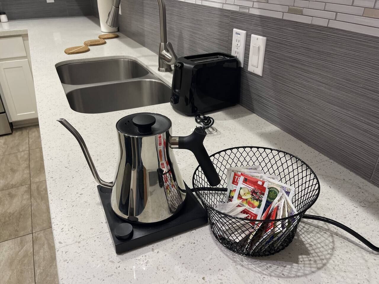 Eine Küche mit einem Edelstahl-Wasserkocher, einem Toaster und einem Korb voller Zeitschriften.