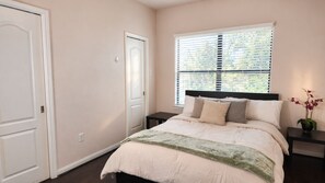 A bedroom with a bed, a nightstand, a window with blinds, and a door. - 2BR/2BA Near NRG, Galleria & Memorial City (Houston)