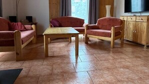 Ein Wohnzimmer mit Holzboden, zwei Sofas, einem Couchtisch, einem Fernseher und einem Fenster mit Vorhängen.