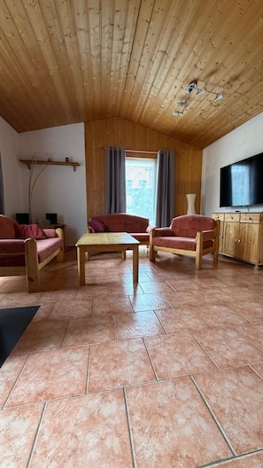 Ein Wohnzimmer mit Holzboden, zwei Sofas, einem Couchtisch, einem Fernseher und einem Fenster mit Vorhängen.