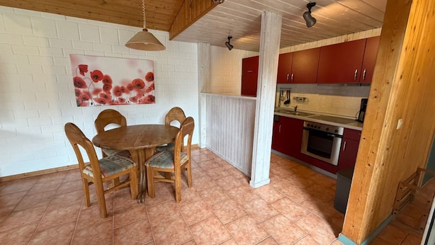 Ein Essbereich mit Holztisch und -stühlen, eine rote Küche mit Schränken und einem Backofen und eine weiße Backsteinwand mit einem Pop-Art-Gemälde.