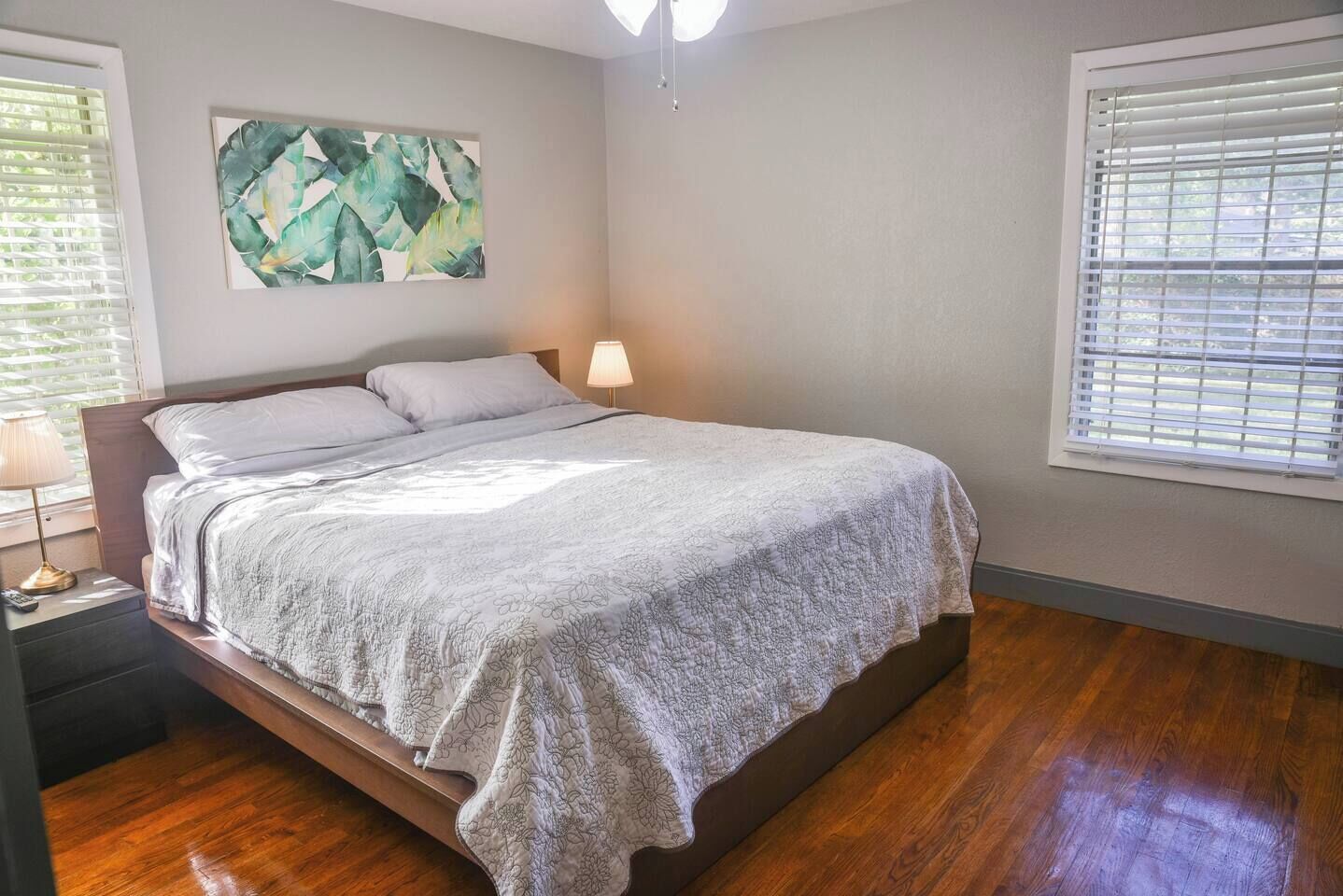 A bedroom with a bed, a nightstand, a wall-mounted lamp, and a window with blinds.