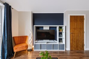 A living room with a flat-screen TV, a wooden door, and a plant on the floor. - Stunning 2BDR 2Bath Salford Apartment with Parking (Greater Manchester)