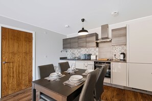 A modern kitchen with a dining area, featuring a wooden door, a table set for two, and a built-in oven. - Stunning 2BDR 2Bath Salford Apartment with Parking (Greater Manchester)