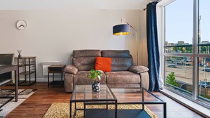 A modern living room with a sofa, coffee table, and a view of the city through large windows. - Stunning 2BDR 2Bath Salford Apartment with Parking (Greater Manchester)