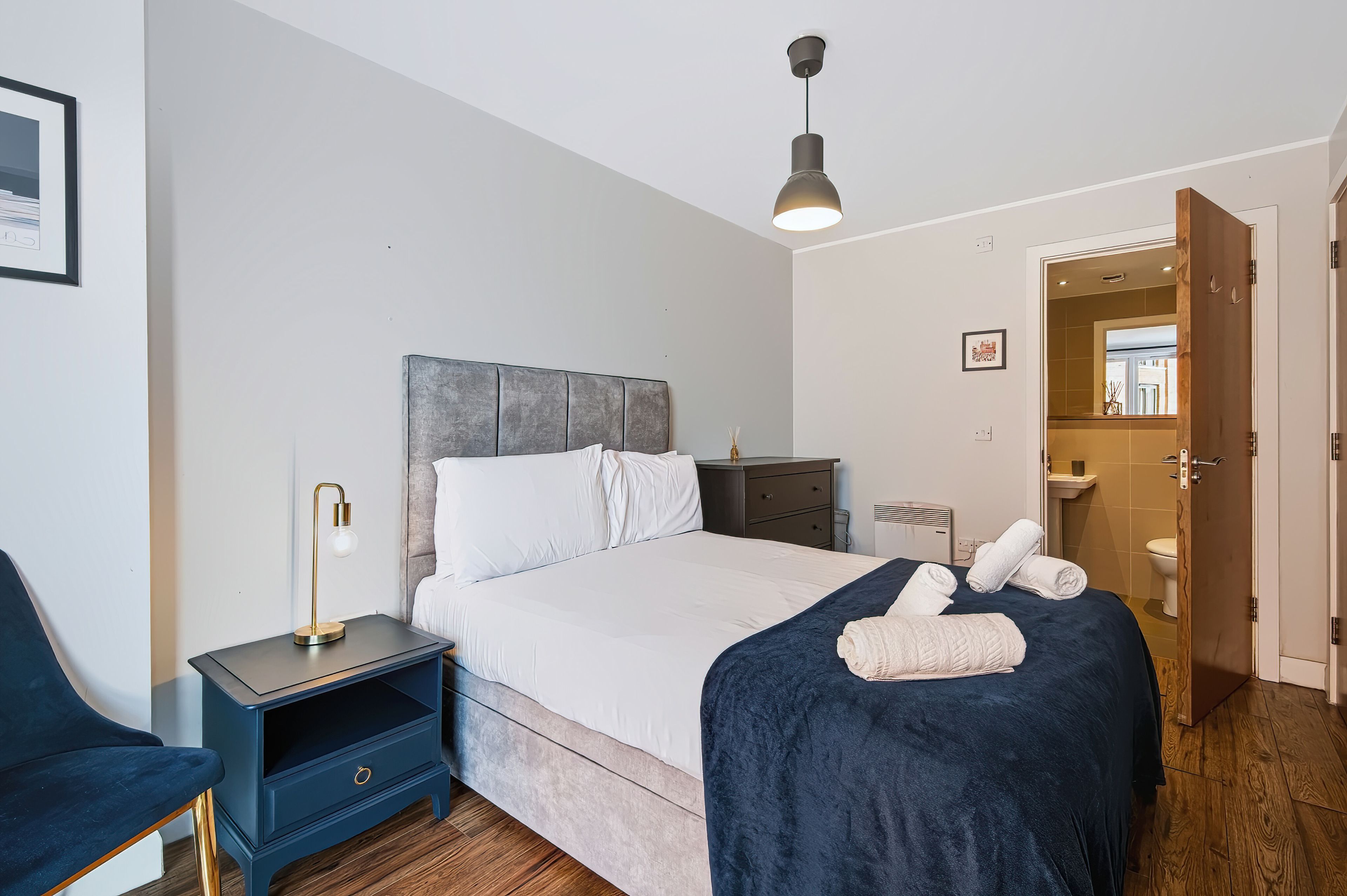 Een moderne slaapkamer met een bed, nachtkastje, lamp en uitzicht op de badkamer.