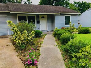 A residential house with a front porch, a pathway leading to the entrance, and various shrubs and flowers. - Family-Friendly Houston Stay Near NRG Stadium (Houston)