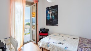 Et soveværelse med seng, stol, skrivebord med hovedtelefoner, et billede og udsigt gennem en skydedør.