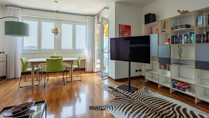 En moderne stue med spiseplads, et fladskærms-tv, en reol og en måtte med zebra-mønster.