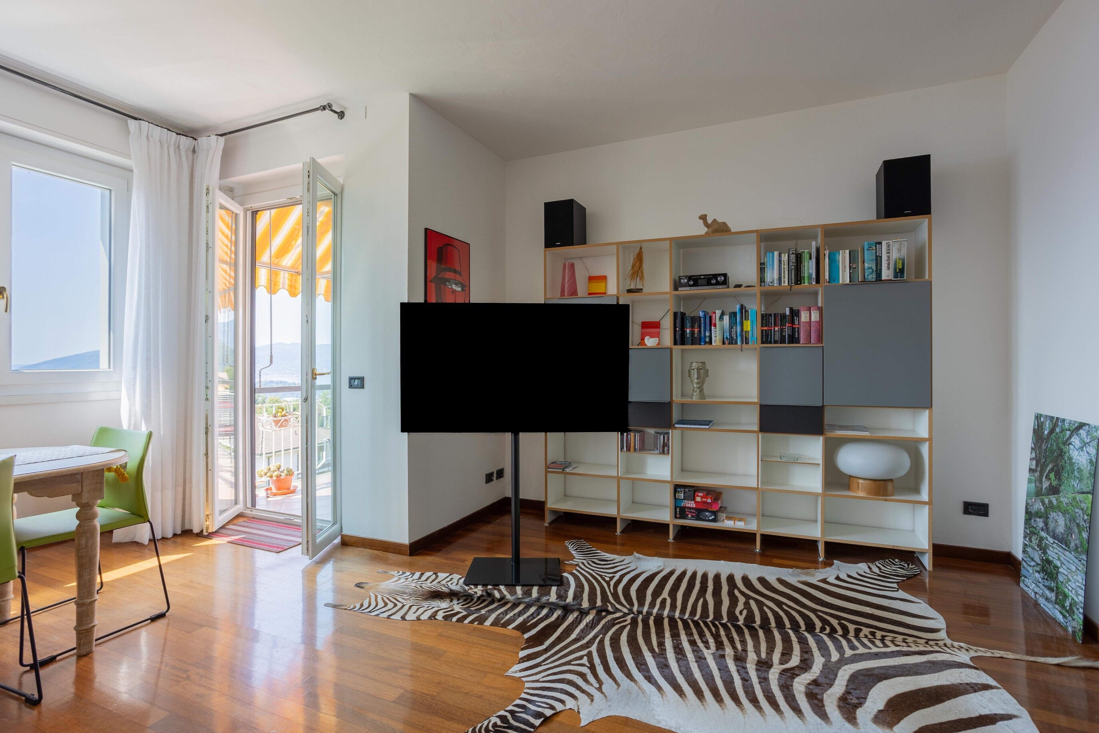 Una sala de estar moderna con un televisor de pantalla plana, un tapete estampado de cebra, una estantería de madera y un comedor con mesa y sillas.