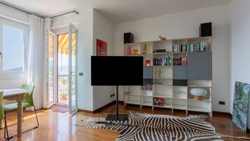 Una sala de estar moderna con un televisor de pantalla plana, un tapete estampado de cebra, una estantería de madera y un comedor con mesa y sillas.