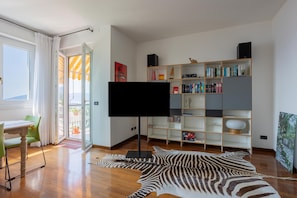 Una sala de estar moderna con un televisor de pantalla plana, un tapete estampado de cebra, una estantería de madera y un comedor con mesa y sillas.