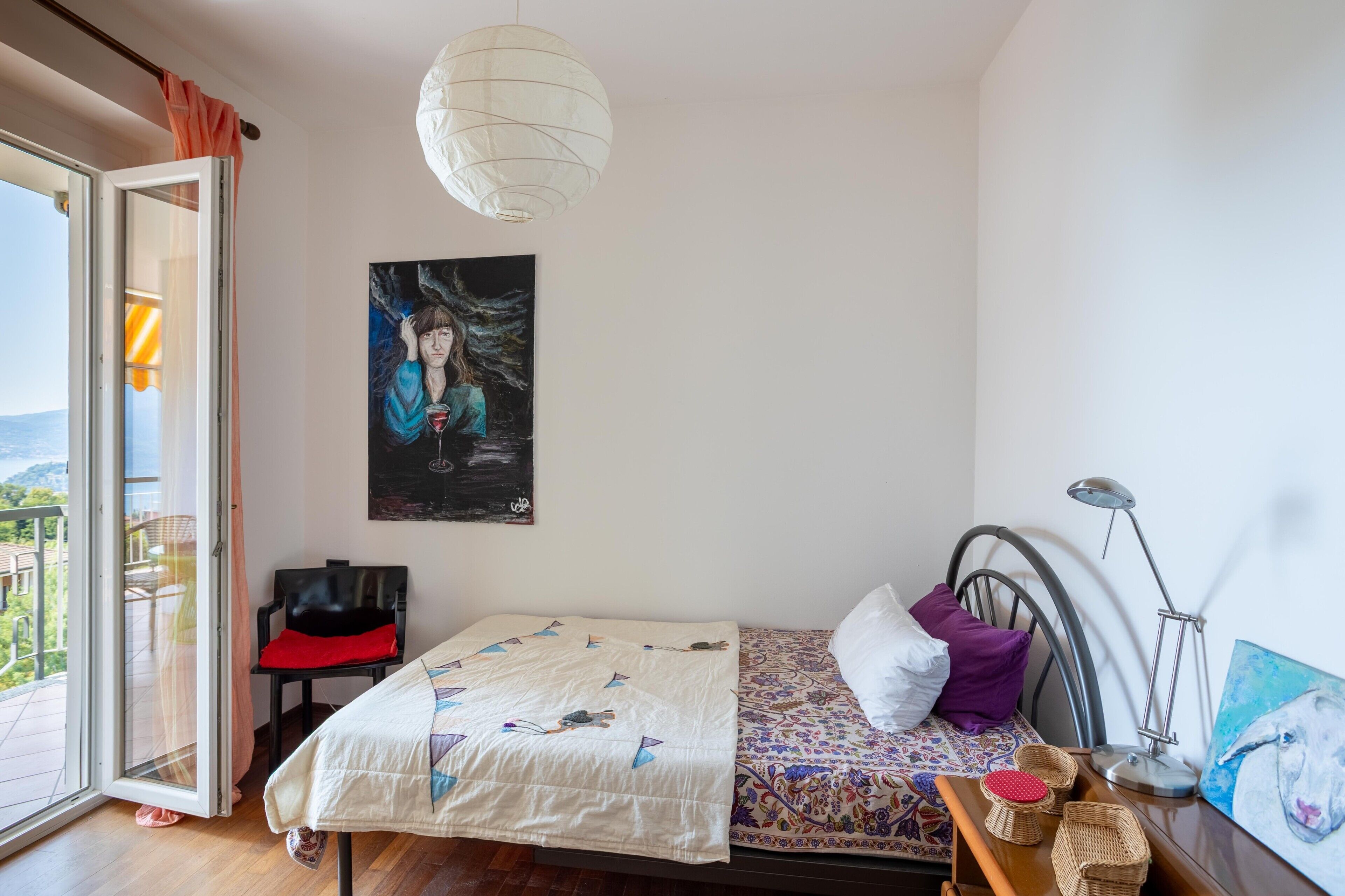 Una camera da letto con un letto, una sedia, una scrivania con una lampada, un quadro e vista panoramica attraverso una porta in vetro.