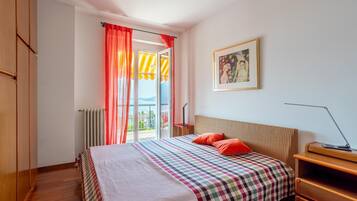 Un dormitorio con cama, mesita de noche, lámpara, radiador, ventana con cortinas y un cuadro en la pared.