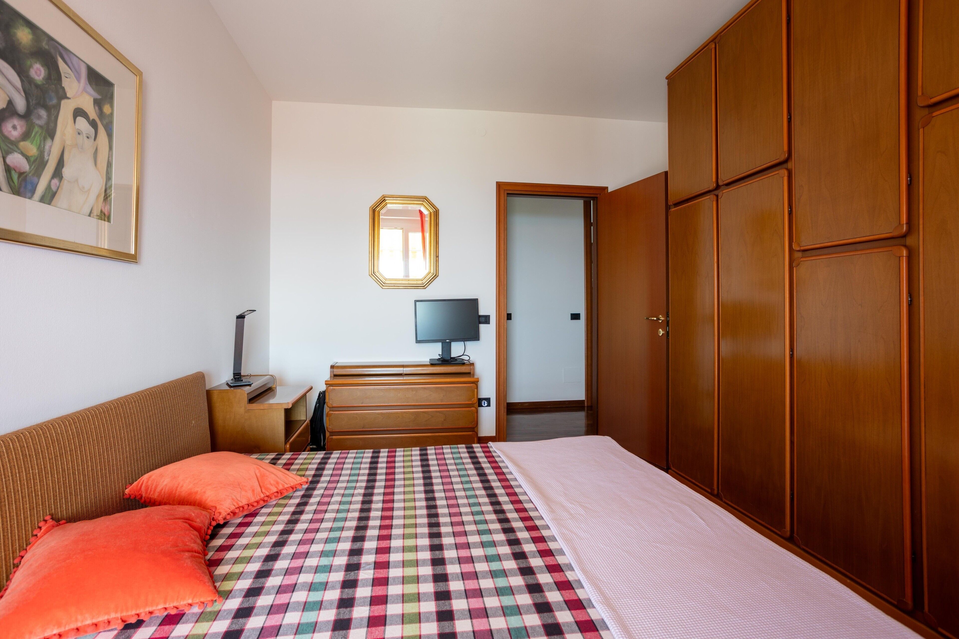 Una camera da letto con un letto, una cassettiera, una scrivania, una sedia, un armadio e un quadro appeso al muro.
