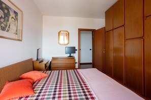 Un dormitori amb un llit, una petita taula de nit, un escriptori, una cadira, un armari i un quadre a la paret.