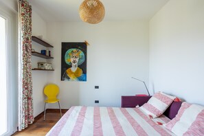 Un dormitorio con una cama, una silla, un cuadro y una estantería con libros.