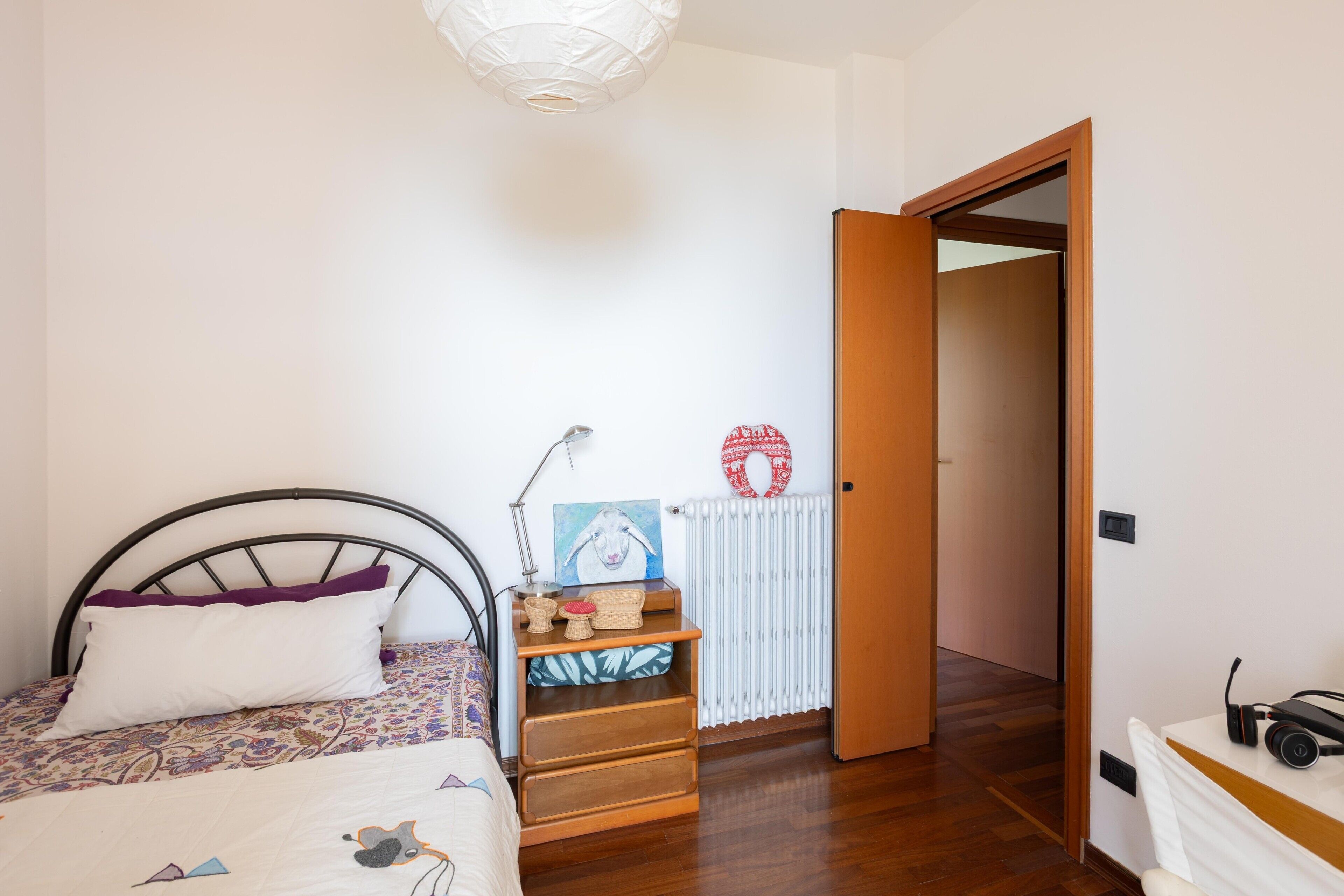 Een slaapkamer met een bed, nachtkastje, lamp en een radiator.