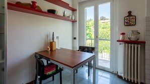 Et køkken med et træbord, stole, røde hylder med køkkenudstyr, en radiator og en dør, der fører ud til en balkon.