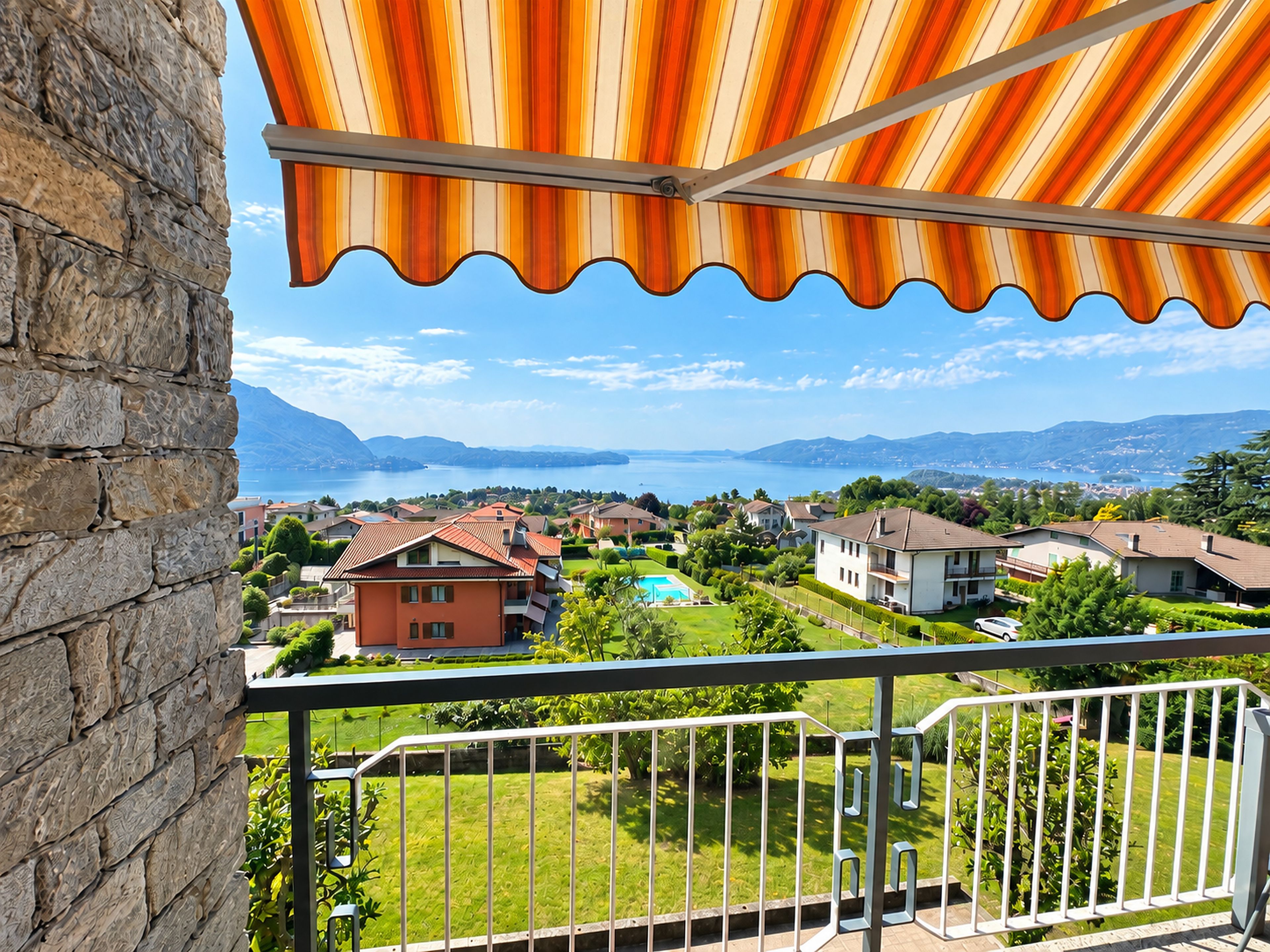 Un balcón con vistas a una zona residencial, una piscina y montañas a lo lejos.