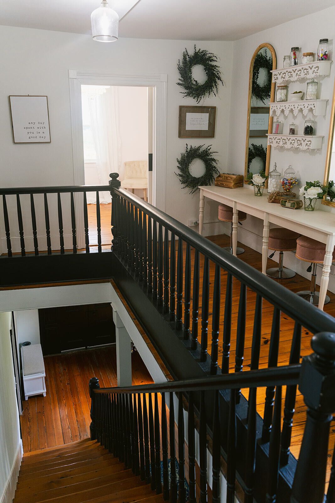 A staircase with a black railing leading to a second floor, a white door, and a wall with decorative wreaths and a mirror.