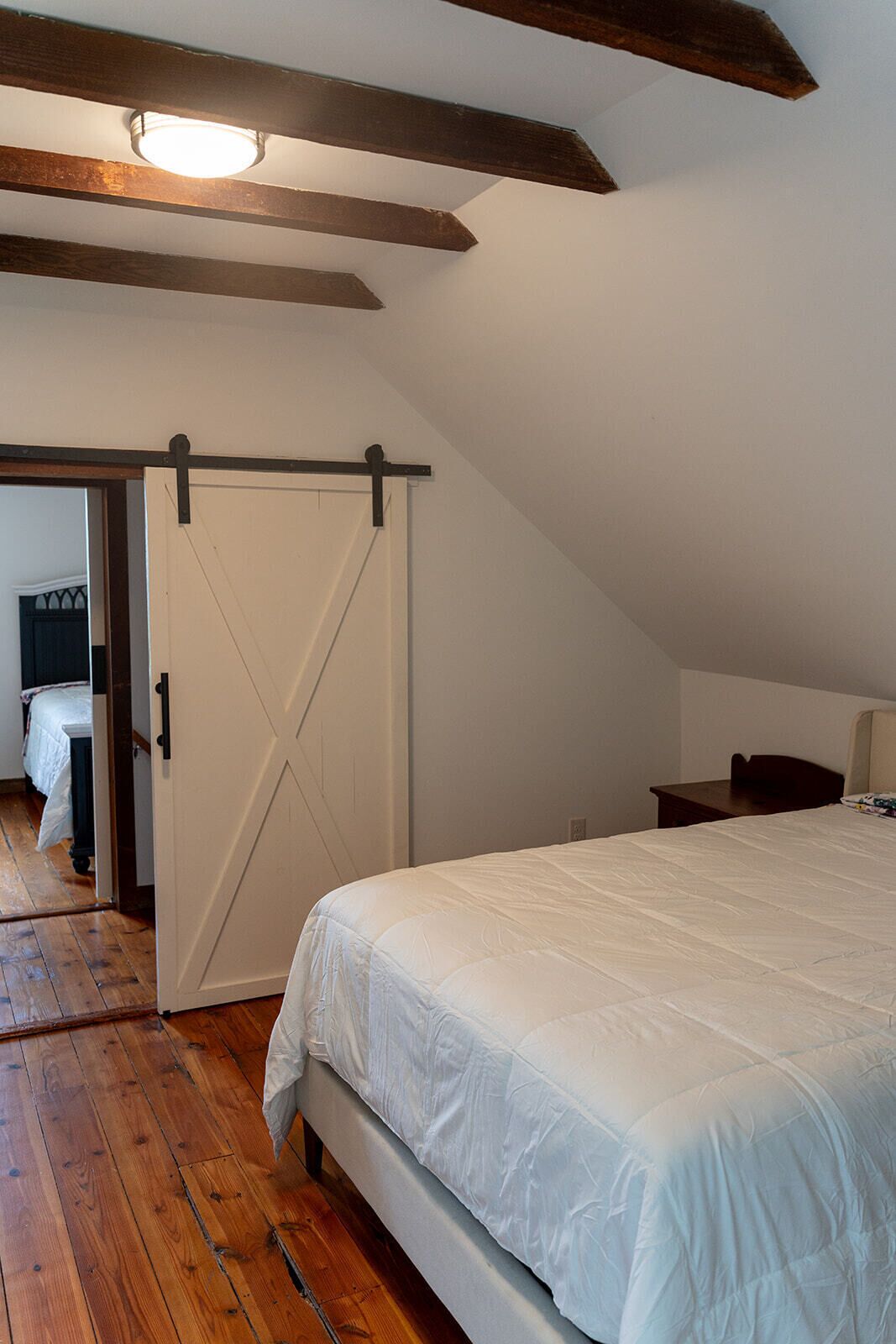 A bedroom with a large bed, wooden flooring, a white door, and a sloped ceiling with exposed beams.