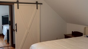 Una camera da letto con un letto grande, pavimento in legno, una porta bianca e un soffitto spiovente con travi a vista.