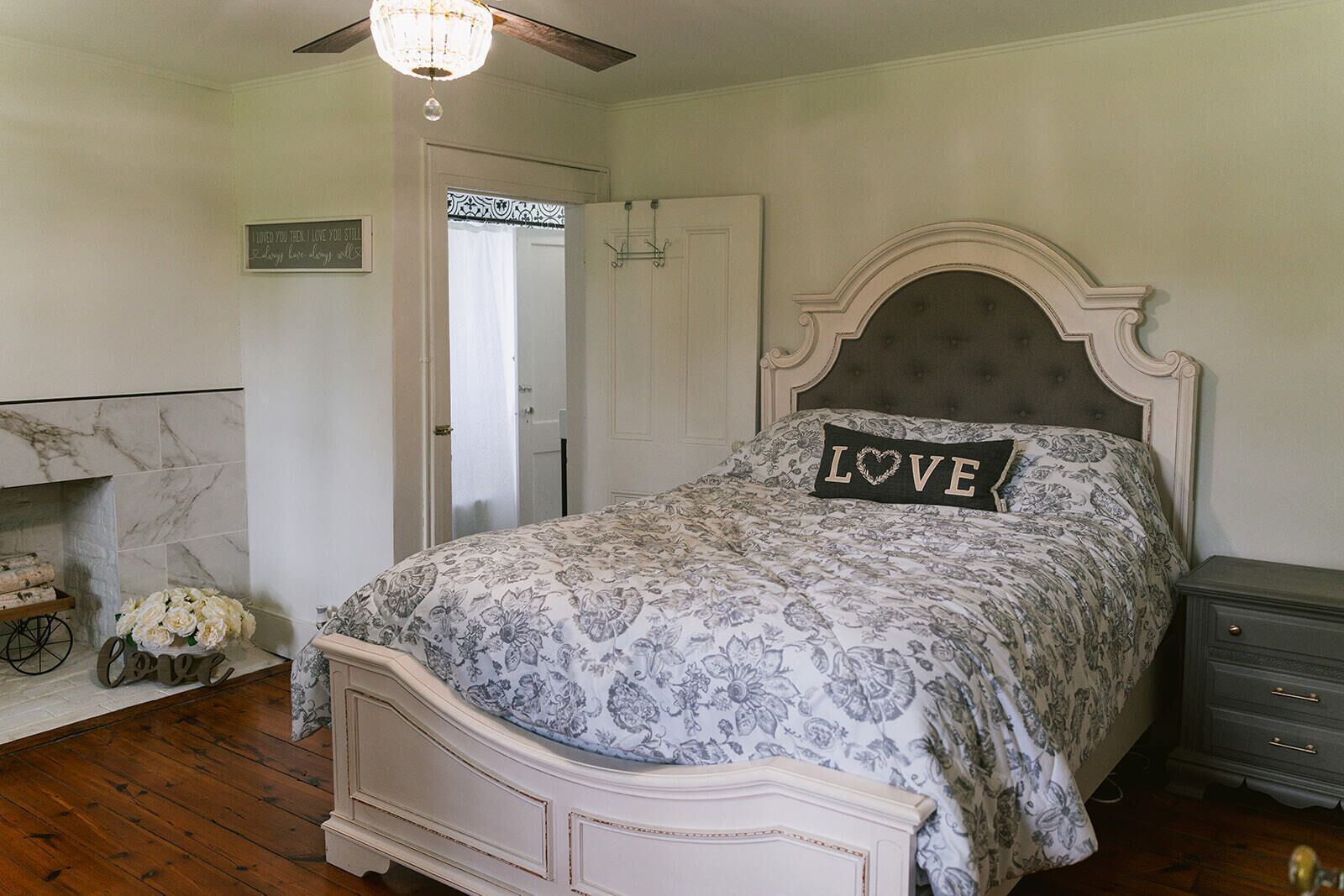 A bedroom with a bed, a nightstand, a dresser, a door, and a chandelier.